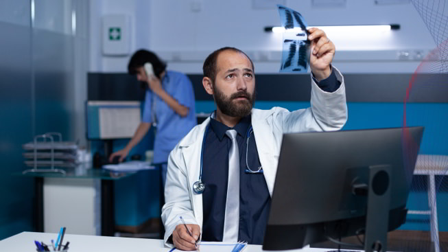 A person in a white coat holding an x-ray