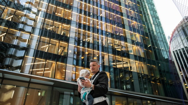 A person holding a baby and mobile phone in front of a glass hotel building