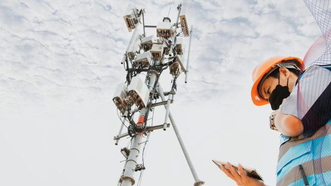 A male engineer standing next to a telecommunication tower against a cloudy sky