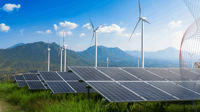 Photovoltaic modules solar power plant with wind turbines against mountains landscape and blue sky with clouds