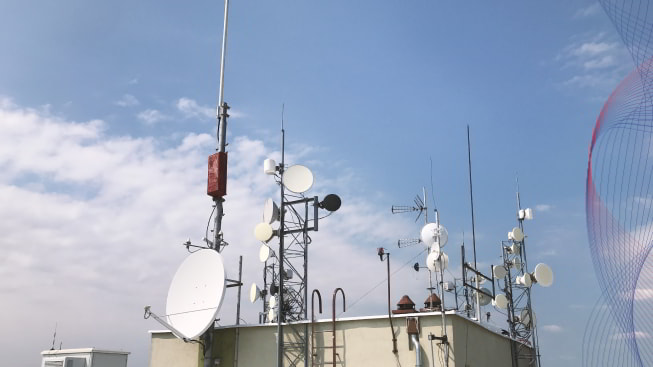 A set of different antennas on the roof of the warehouse against cloudy background