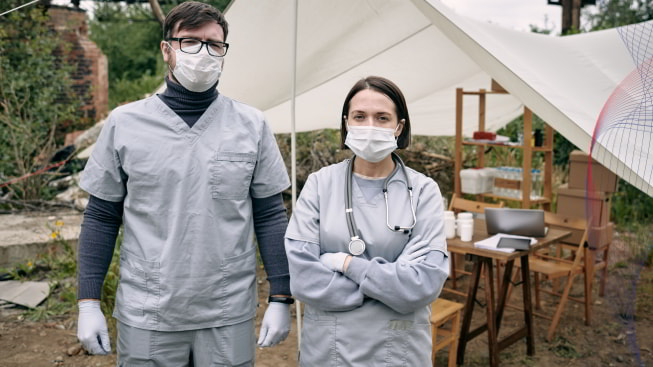 Medical workers in masks and scrubs standing against tent with medicine