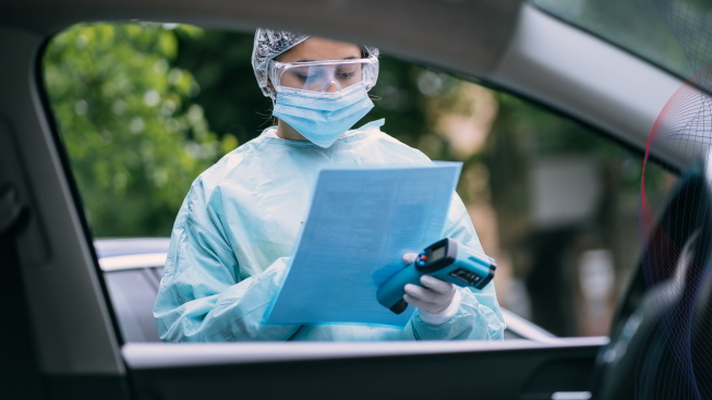 Nurse wears a protective suit and mask during drive thru parking lot health testing